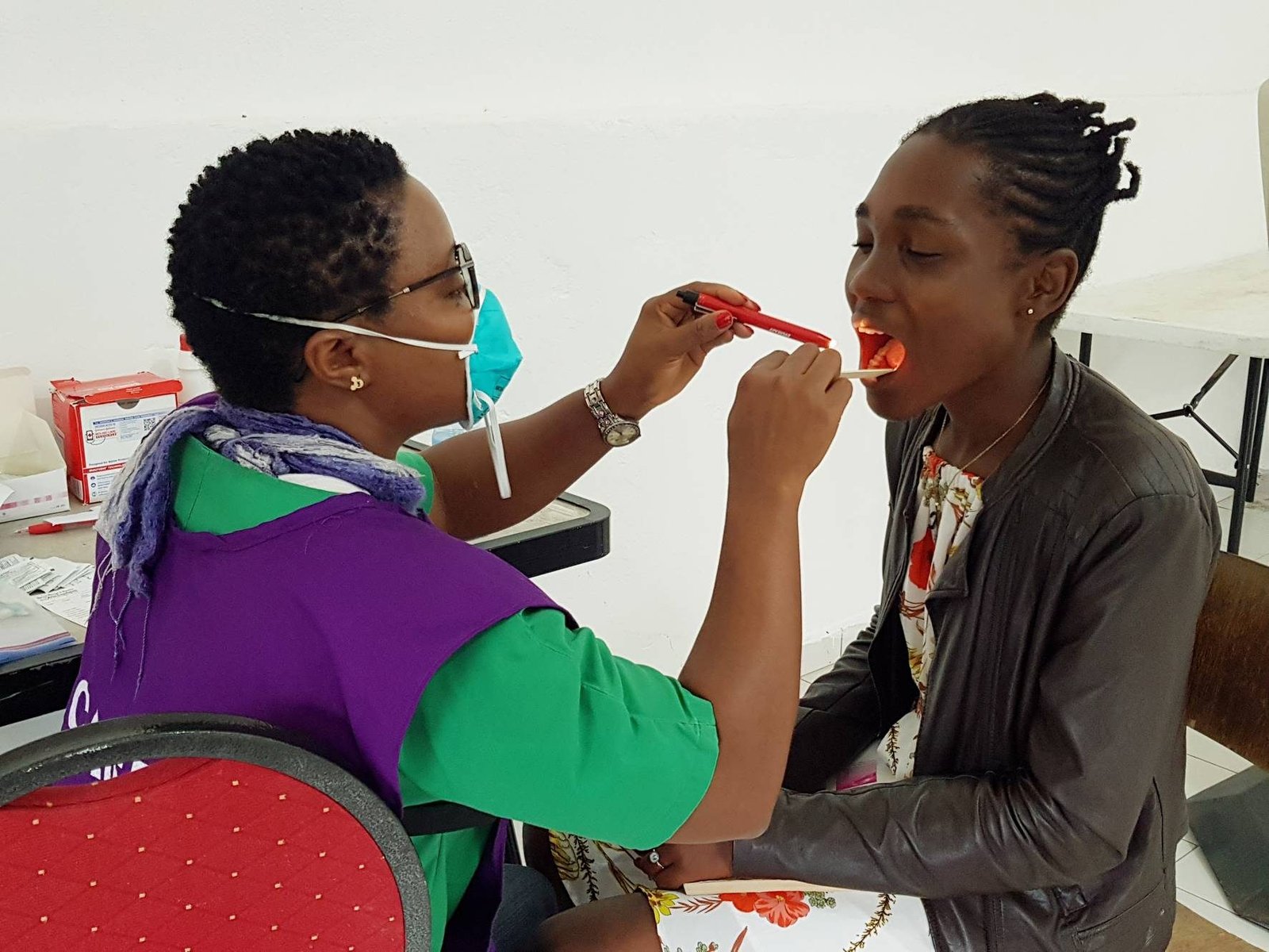 A volunteer in a purple apron examining a patient's mouth