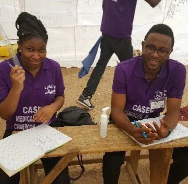 Two smiling volunteers in purple shirts with paperwork