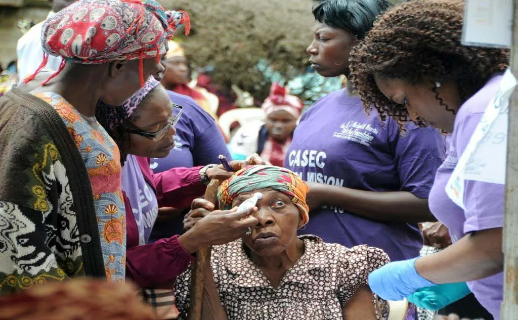 A volunteer examining an elderly woman's eye while others wait