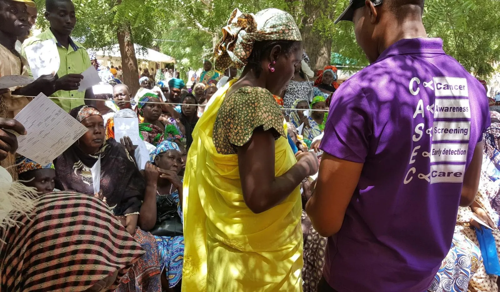 A volunteer in a purple CASEC shirt registering a woman in a large crowd