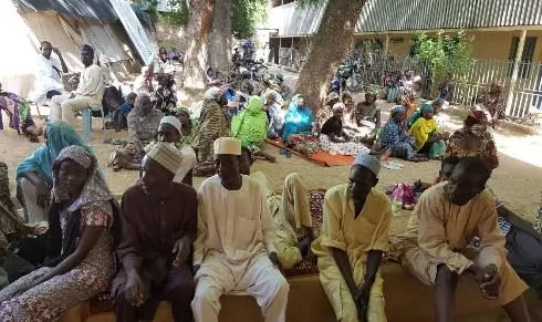 Men waiting on benches in the shade of trees