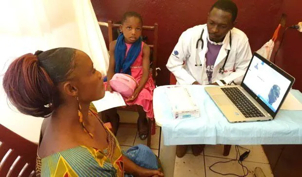 A doctor at a laptop consulting a mother and child