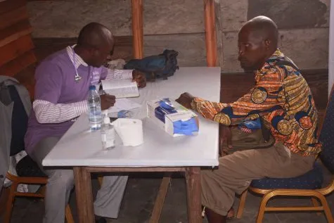 A doctor and a volunteer consulting a patient across a table
