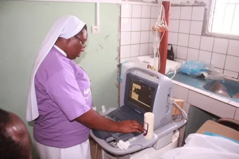 A nun in a lilac mission shirt operating an ultrasound machine