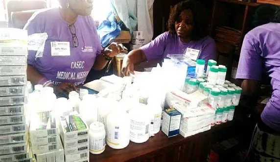 Volunteers in purple shirts sorting medicine at the pharmacy table
