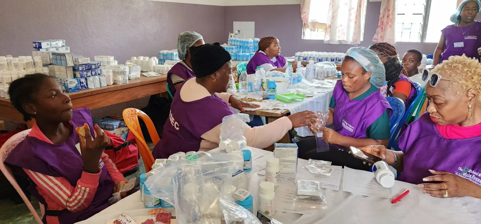 Volunteers in purple mission aprons working with patients at long tables
