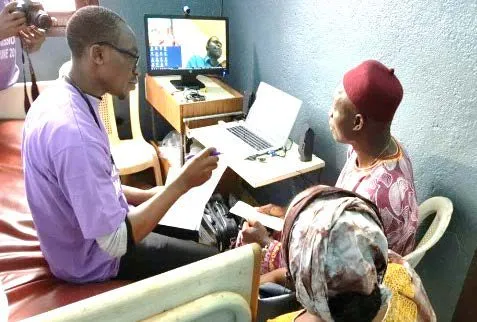 A volunteer and a patient on a video call with a remote doctor