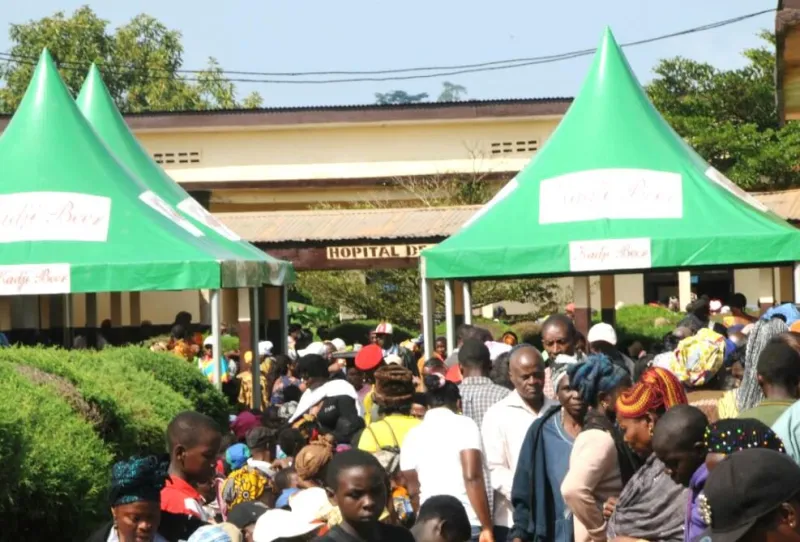 A large crowd under green tents outside a district hospital