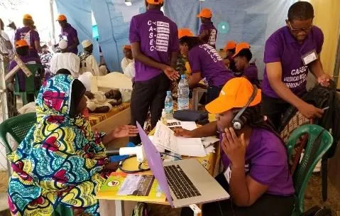 A volunteer with a laptop in a busy clinic tent