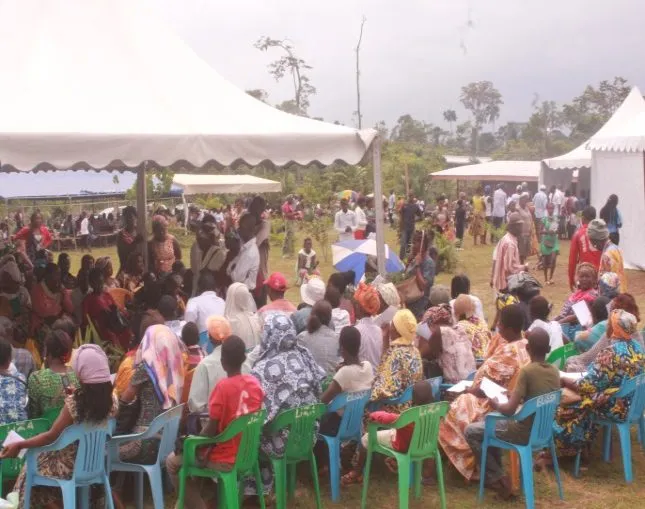 Patients seated on green and blue plastic chairs under white tents