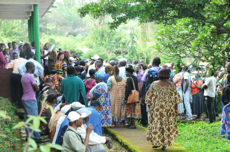 People gathered in front of a hospital surrounded by trees