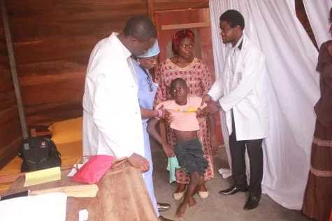 Two doctors in white coats examining a young girl with her mother