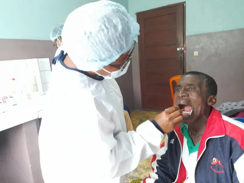 A dentist in white protective gear examining a man's teeth